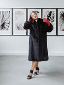 Woman wearing a black fur coat with red gloves in a room with abstract wall art.
