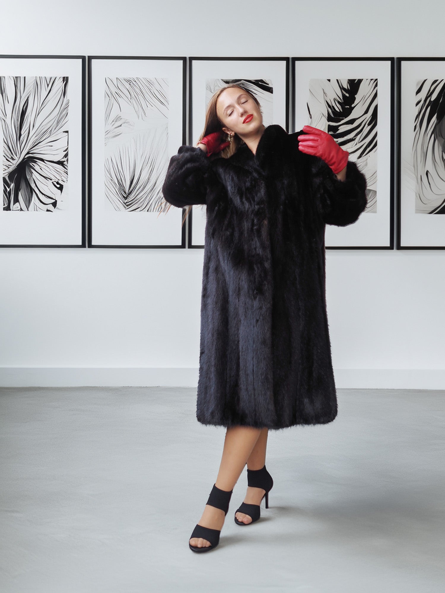 Woman wearing a black fur coat with red gloves in a room with abstract wall art.