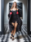 Woman in black dress and red boxing gloves standing in a room with checkered floor and mirror.