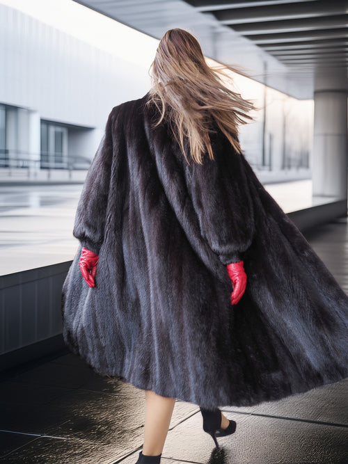 Person wearing a long dark coat and red gloves walking away in an urban setting.