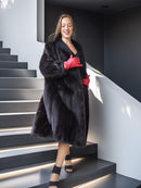 Woman in a black fur coat and red gloves standing on a modern staircase.