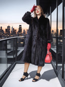 Woman in a black fur coat and red gloves standing on a rooftop with a cityscape background