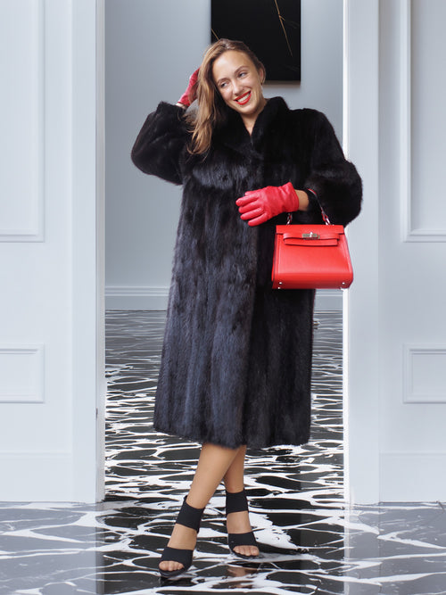 Woman in a black fur coat and red gloves holding a red handbag in a stylish interior setting.