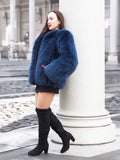 Elegant blue fox fur jacket with a soft crew neck, styled with a red handbag. A sophisticated winter coat for a bold fashion statement.