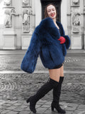 Elegant blue fox fur coat with a soft crew neck, styled with red gloves. A statement winter fashion piece for sophisticated style.