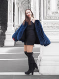 Elegant blue fox fur jacket with a soft crew neck, styled with a red handbag. A sophisticated winter coat for a bold fashion statement.