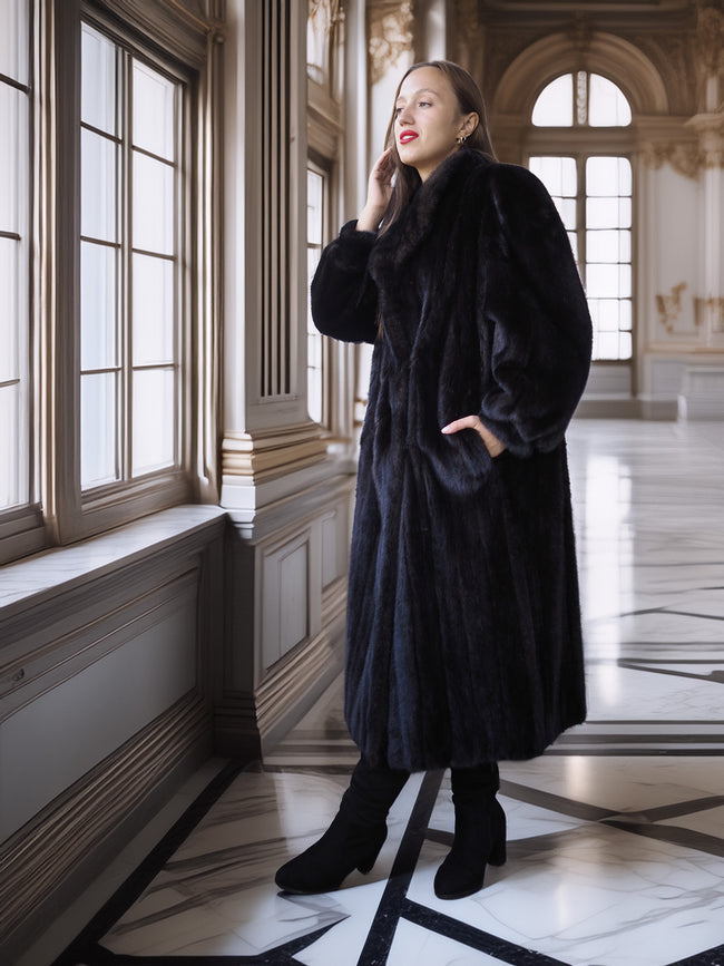 Woman in a black fur coat standing in an elegant interior setting with large windows.