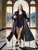 Woman in a long black coat standing in a room with large windows showing a scenic view.