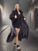 Woman in a long dark fur coat and black dress standing on a stone street.