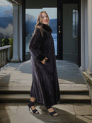 Woman in a long dark coat standing on a stone porch with a scenic background