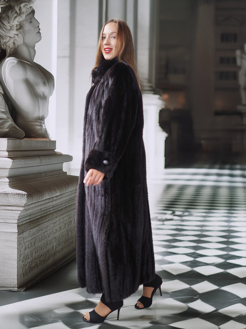 Woman in a long black coat standing in an elegant interior setting with checkered floor and classical sculpture.