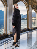 Woman in a dark coat standing in an elegant interior with a lake view.