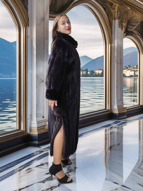 Woman in a dark coat standing in an elegant interior with a lake view.