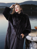 Woman wearing a black fur coat by a lakeside with mountains in the background