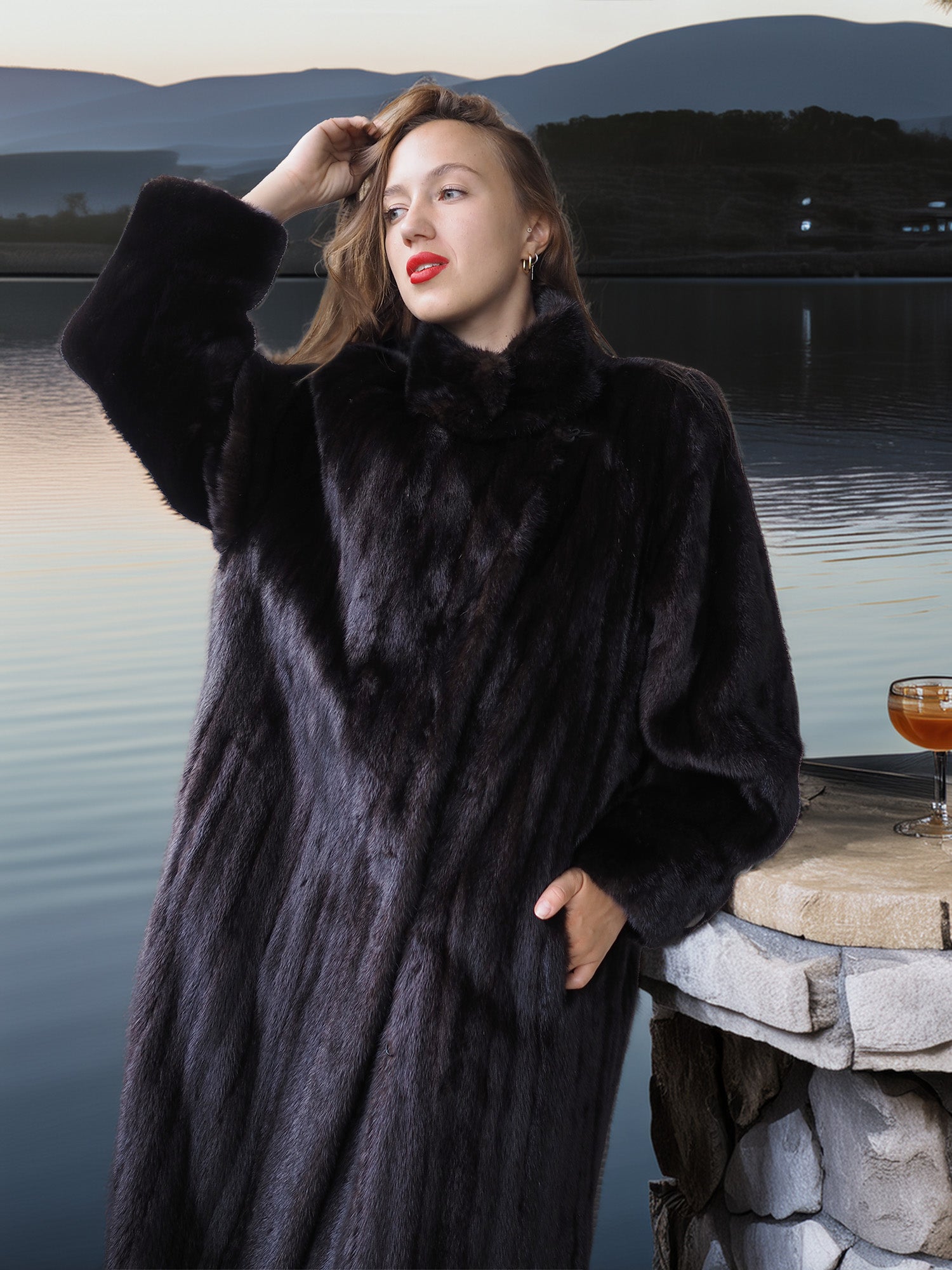 Woman wearing a black fur coat by a lakeside with mountains in the background