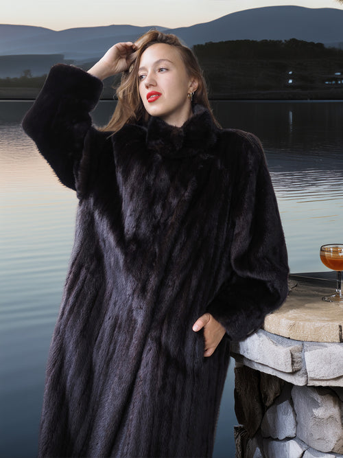 Woman wearing a black fur coat by a lakeside with mountains in the background