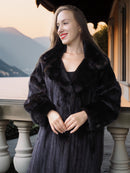 Woman wearing a dark fur coat standing on a balcony with scenic background