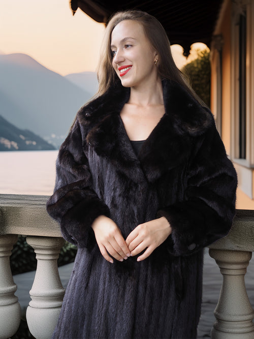 Woman wearing a dark fur coat standing on a balcony with scenic background