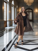 Woman in a brown fur coat standing in an elegant interior setting with marble floors and high ceilings.