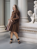 Woman in a brown fur coat standing in an elegant interior setting with classical statues.