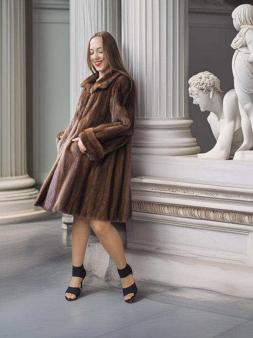 Woman in a brown fur coat standing in an elegant interior setting with classical statues.