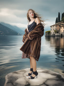Woman in a fur coat standing on a rock with a lake and mountains in the background