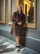 Woman in a brown fur coat standing in a room with decorative walls and framed pictures.