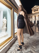 Woman in a black dress and fur coat standing in an elegant interior setting with classical architecture.