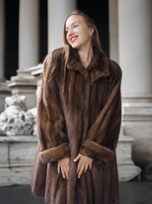 Woman wearing a brown fur coat standing in front of classical architecture.