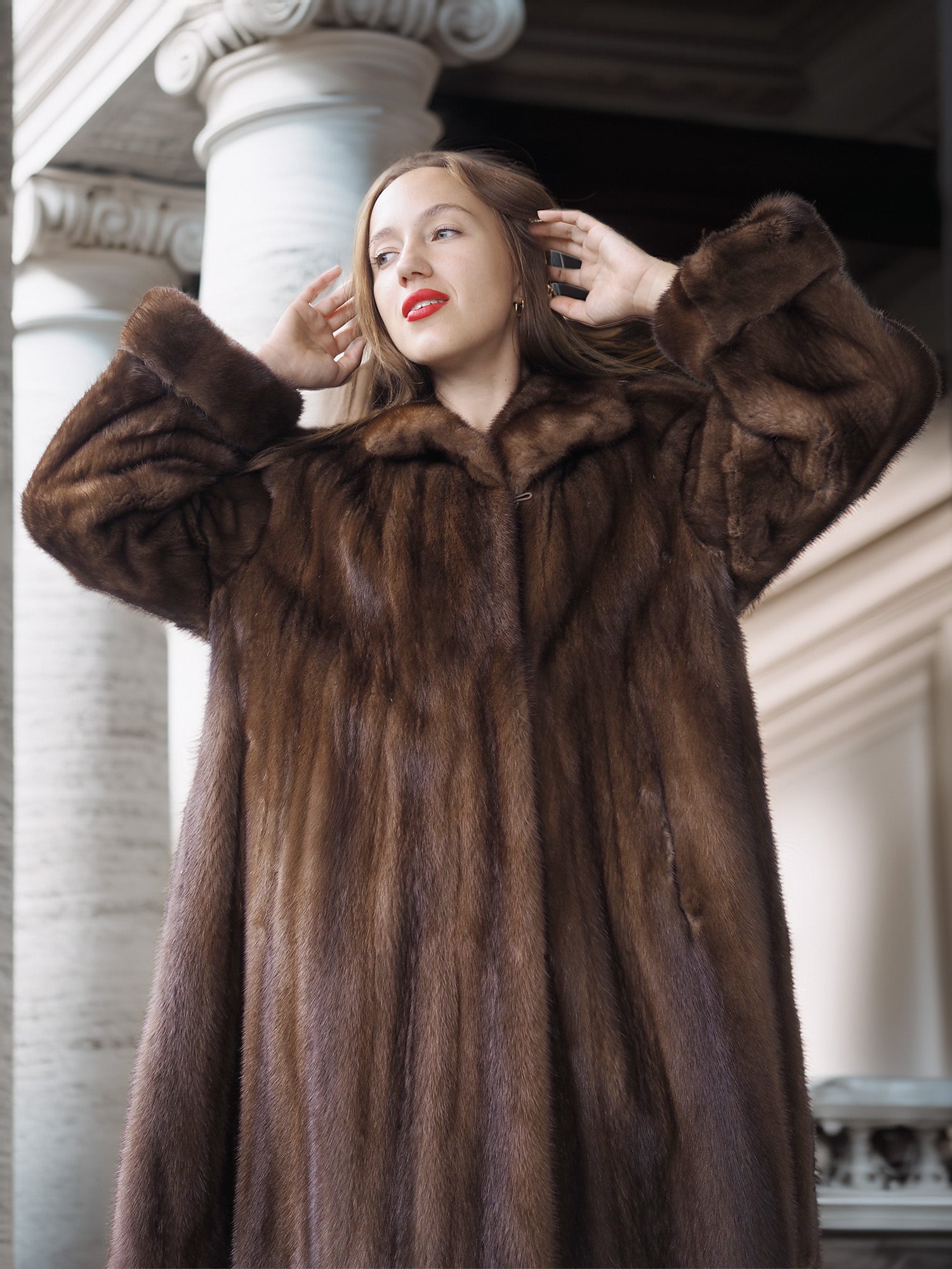 Woman wearing a fur coat standing in front of classical architecture.