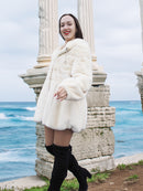 Beige Pearl Mink Fur Coat with hood, worn by a woman near ancient ruins by the sea. Features hook-eye closure, satin lining, and elegant warmth.