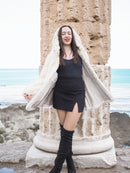 Elegant Beige Pearl Mink Fur Coat with hood, worn by a model near ancient ruins overlooking the sea. Luxurious warmth with hook-eye closure and satin lining.