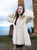 Beige Pearl Mink Fur Coat with hood, worn by a woman near ancient ruins. Luxurious warmth with hook-eye closure, satin lining, and elegant design.