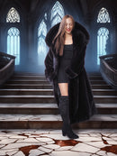 Woman in a long black coat standing on a staircase with stained glass windows in the background