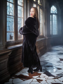 Woman in a long dark fur coat standing in a room with stained glass windows.