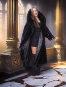 Woman in a long black fur coat standing in an ornate room with gold columns and marble floor.
