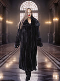 Woman wearing a long black fur coat in an elegant hallway with chandeliers.