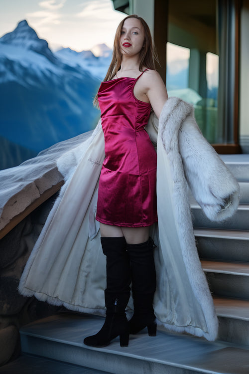 Woman in a pink dress and black boots standing on a balcony with mountains in the background