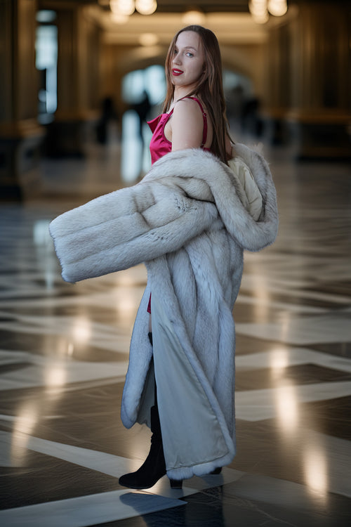 Woman holding a fur coat in an indoor setting with reflective floor and blurred background