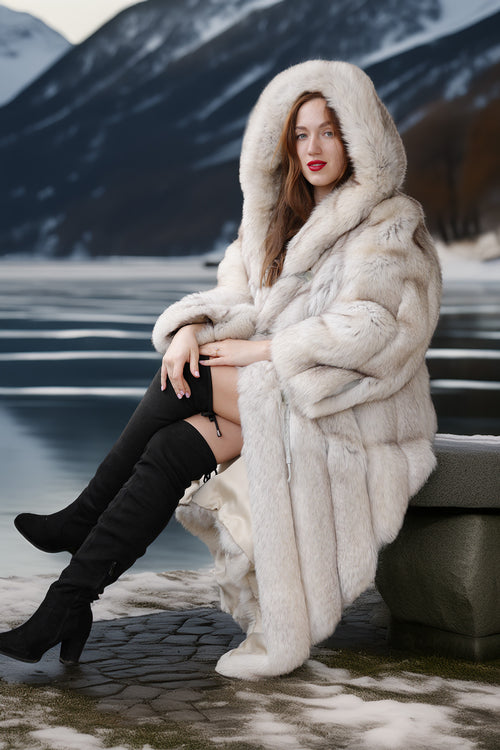 Woman in a fur coat sitting on a rock with mountains in the background