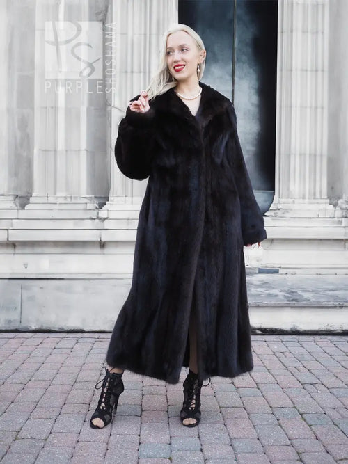 Black mink fur coat with V-front and long sleeves, finger-to-lip pose.