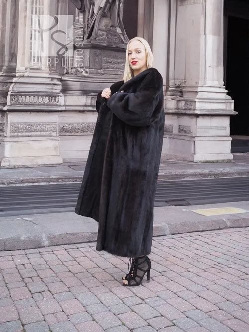 Mink fur coat in dark black with long hem and wide cuffs, side view