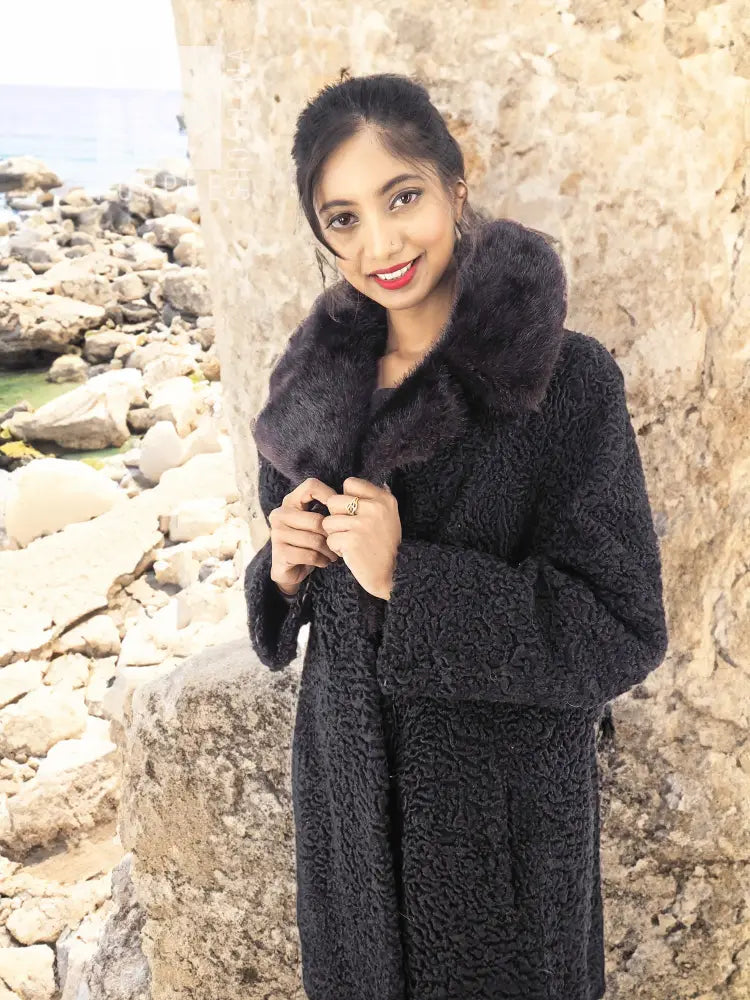 Black Persian lamb coat with mink collar, hands clasped, textured curly fleece front.