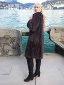 Dark mink fur hooded coat with high collar, standing pose near water