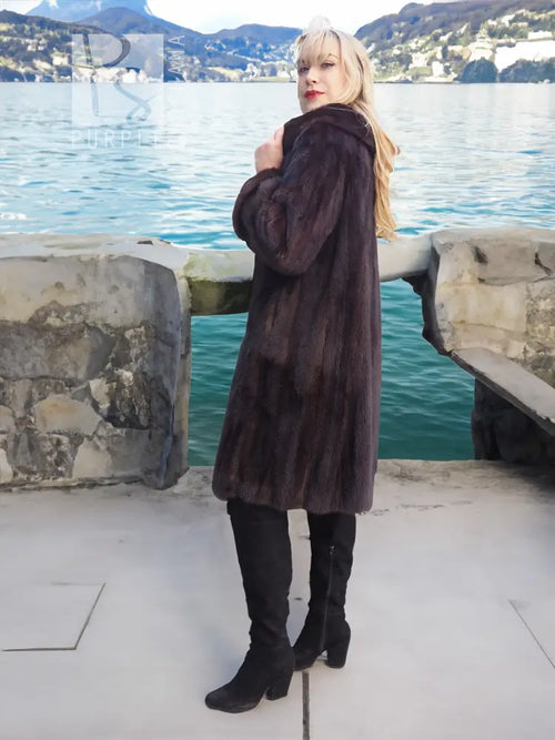 Dark mink fur hooded coat with high collar, standing pose near water