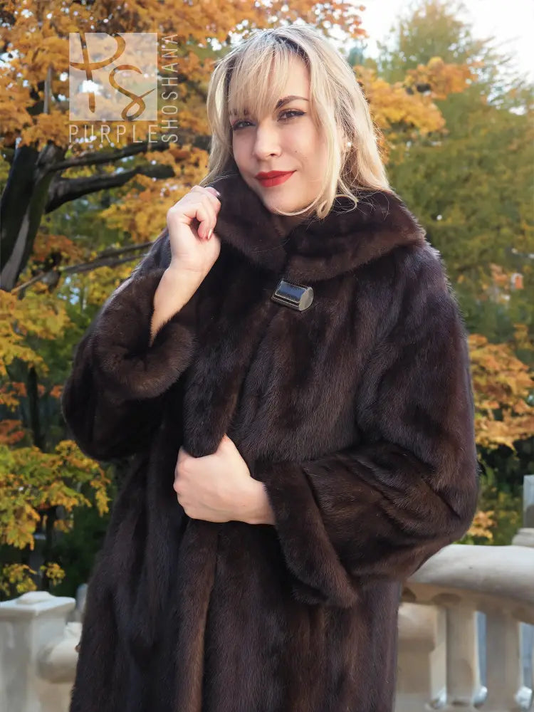 Dark mink fur coat with stand collar, buttoned up and held at the neck
