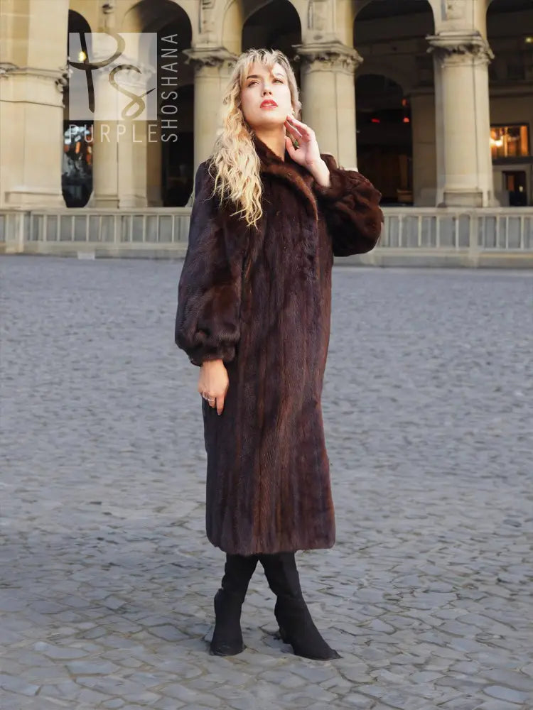 Mahogany-brown mink fur coat with raised collar and fitted sleeves, knee-length over boots.