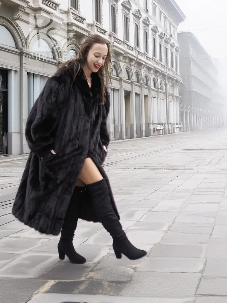 Black mink fur coat, long flared cut with notched collar, worn over dark leggings and boots.