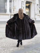 Black mink fur coat from behind, long voluminous hem and wide sleeves; model walking stance.