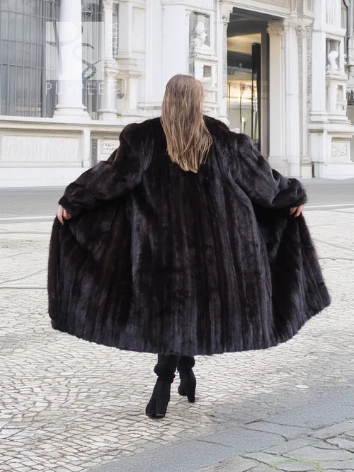 Black mink fur coat from behind, long voluminous hem and wide sleeves; model walking stance.